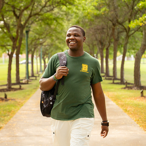 International student and nursing major, Precious Cyril, walking along the Alumni Walk on campus at SUNY Brockport and carrying a backpack.