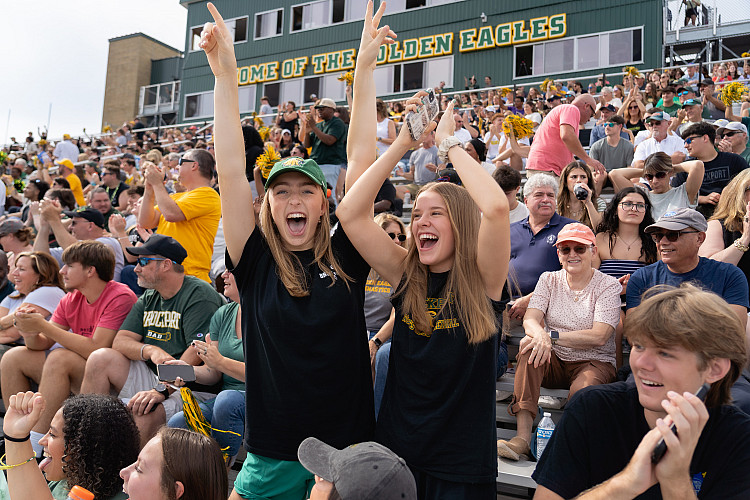 Two students cheering in the bleachers of the Brockport Homecoming football game.