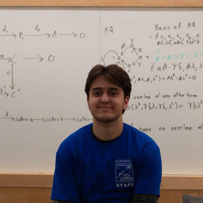 Nicholas Pisano sitting in front of a whiteboard filled with equations