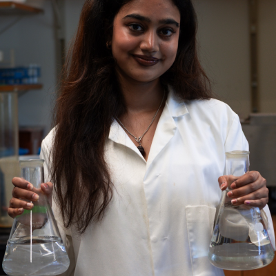Yashaswini Jha dressed in a lab coat in a lab holding glass beakers