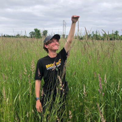 Chris Cammisa playfully measuring tall grass in a grassfield