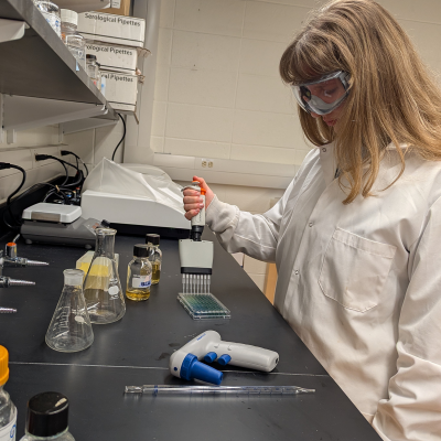 Eileena Frey dressed in lab gear and in a lab handling a special droplet that drops samples into a small tray