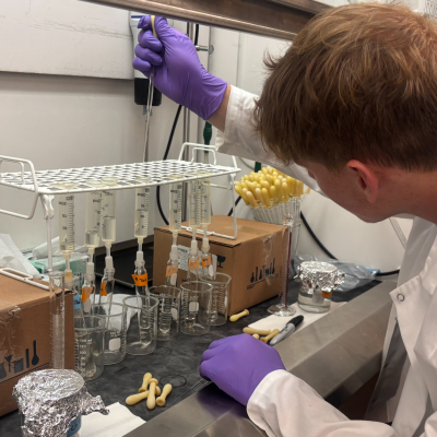 Conner Berger dressed in lab gear in a lab handling a droplet into several glass beakers