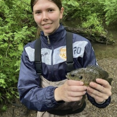 Jessica Freese holding a small fish near a creek