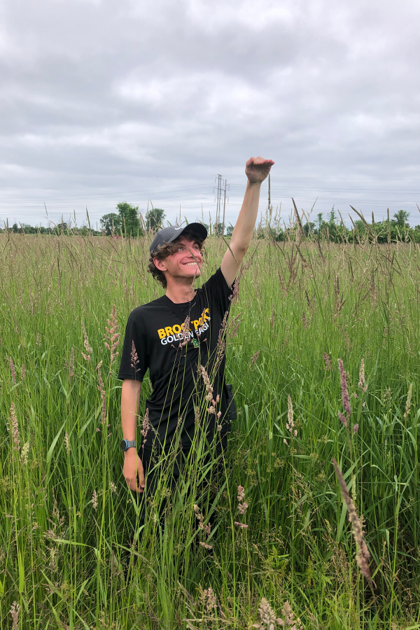 Chris Cammisa playfully measuring tall grass in a grassfield