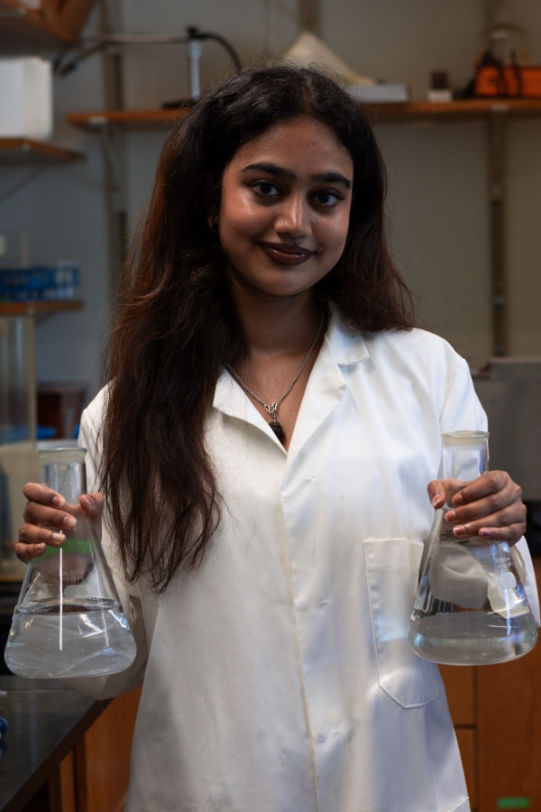 Yashaswini Jha dressed in a lab coat in a lab holding glass beakers