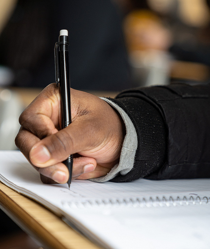 Student writing on a piece of lined paper with a pen