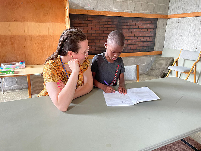 Brockport Summer Learning staff sitting next to a student, who is writing on a notebook.