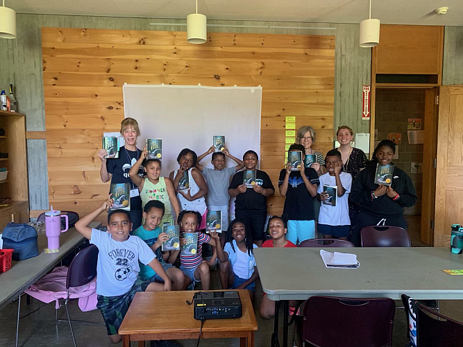 Brockport Summer Learning staff and students holding a copy of The One and Only Ivan and posing for a group photo.