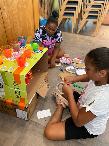 2 Brockport Summer Learning students crafting a cardboard box with plastic cups, ping pong balls, and colored tape.