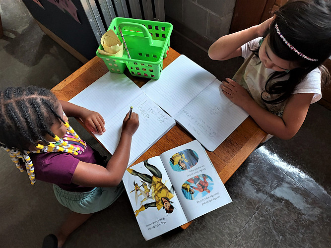 2 children on a table drawing on coloring books