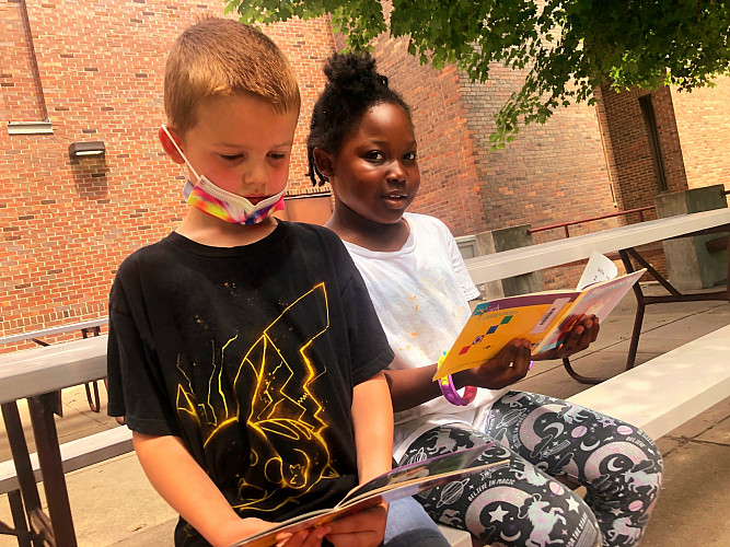 2 children reading books on a picnic table outside