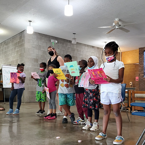 Children lined up with a staff holding up their drawings