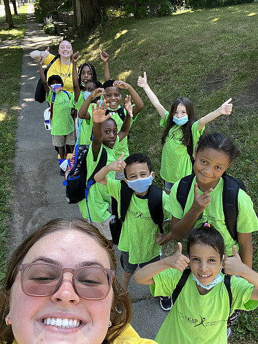 A staff taking a selfie with children in green shirts lined up on a sidewalk
