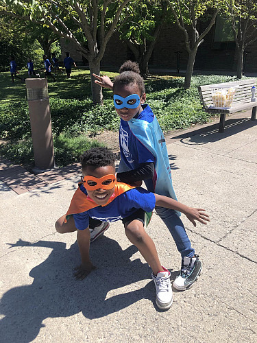 2 children dressed up as superheroes posing for the camera on a sidewalk