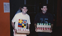 Color snapshot of two men carrying cases of soda.