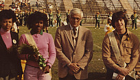 Color photo of homecoming king and queen posing with a college administrator.