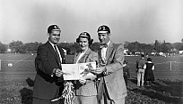 Black and white photo of three people on a football field viewing a homecoming brochure together.