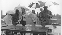 Black and white photo of people standing with umbrellas in the rain.