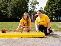 Students kneeling and painting a parking bumper yellow.