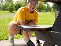 One student, smiling, painting a picnic table at a local park