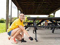 One student, smiling, painting a picnic table at a local park