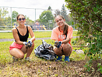 Two volunteers, smiling, picking up trash at a local playground