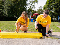 Students kneeling and painting a parking bumper yellow.