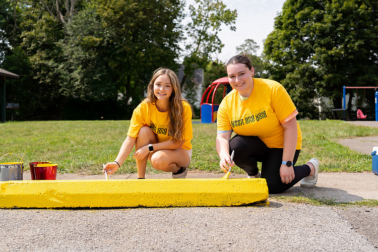 Students kneeling and painting a parking bumper yellow.