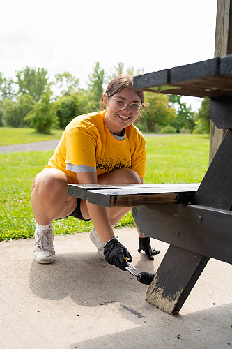 One student, smiling, painting a picnic table at a local park
