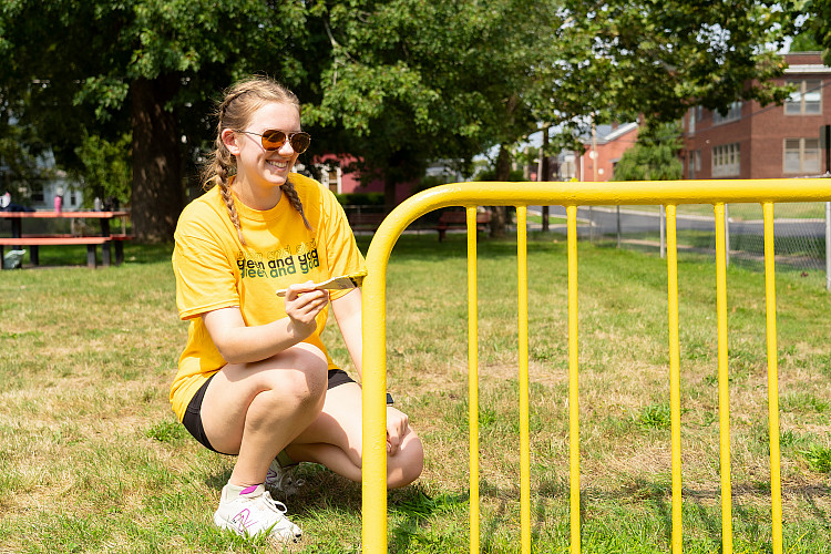 One student, smiling, painting a bike rack at a local park