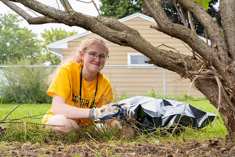 One student volunteer, smiling, picking up trash at a local playground