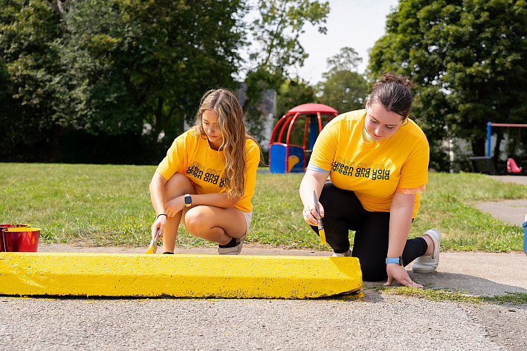 Students kneeling and painting a parking bumper yellow.