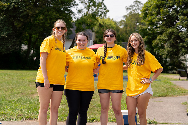 Four students wearing yellow t-shirts standing and smiling during Saturday of Service