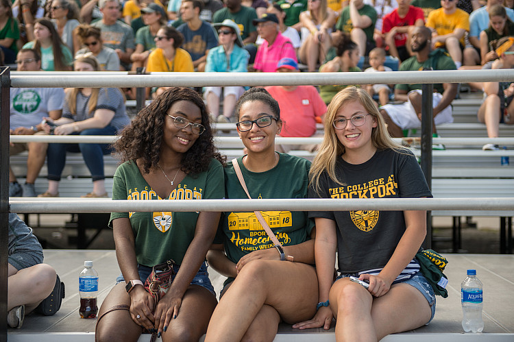 Three alums in bleachers at Homecoming.