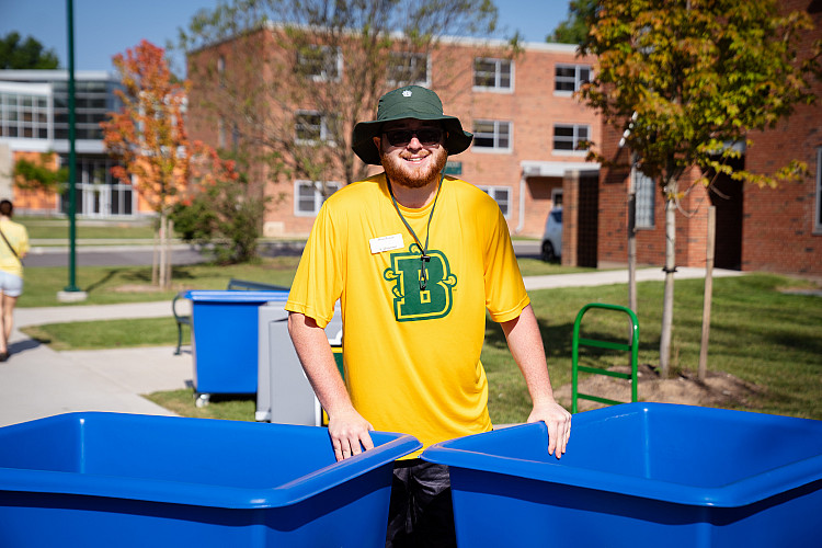 Man wearing bucket hat standing with large blue bins.