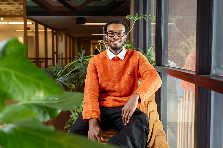 Student sitting inside next to plant.