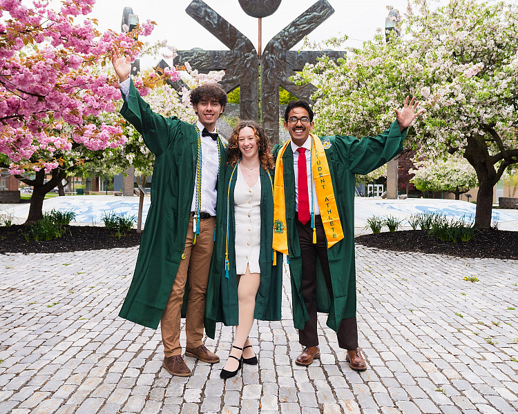Three Brockport students wearing cap and gowns in front of Special Olympics statue.