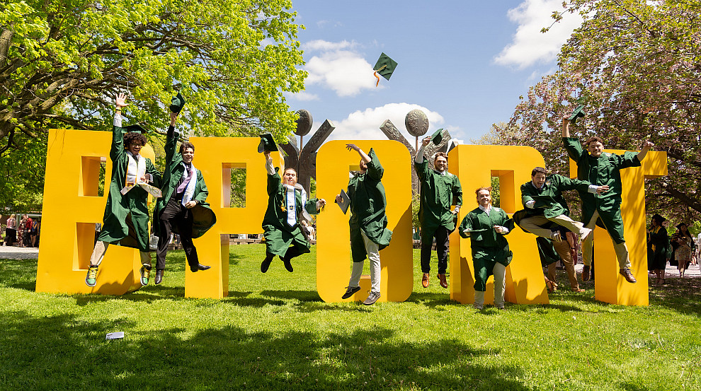 Brockport graduates jumping into air in front of large BPORT letters.