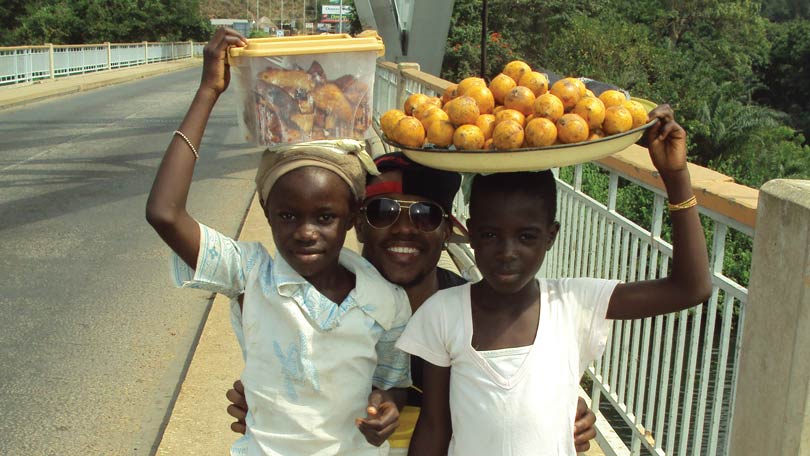 Kids from Ghana carrying food over their heads posing for the camera