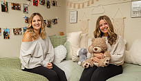 two students pose sitting on their beds in their dorm rooms