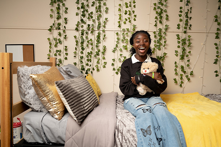 student poses on her dorm room bed holding stuffed animal