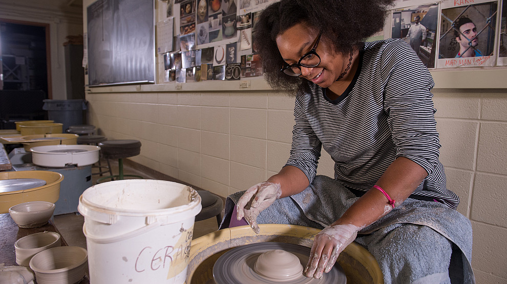 student in pottery studio spinning a pottery wheel