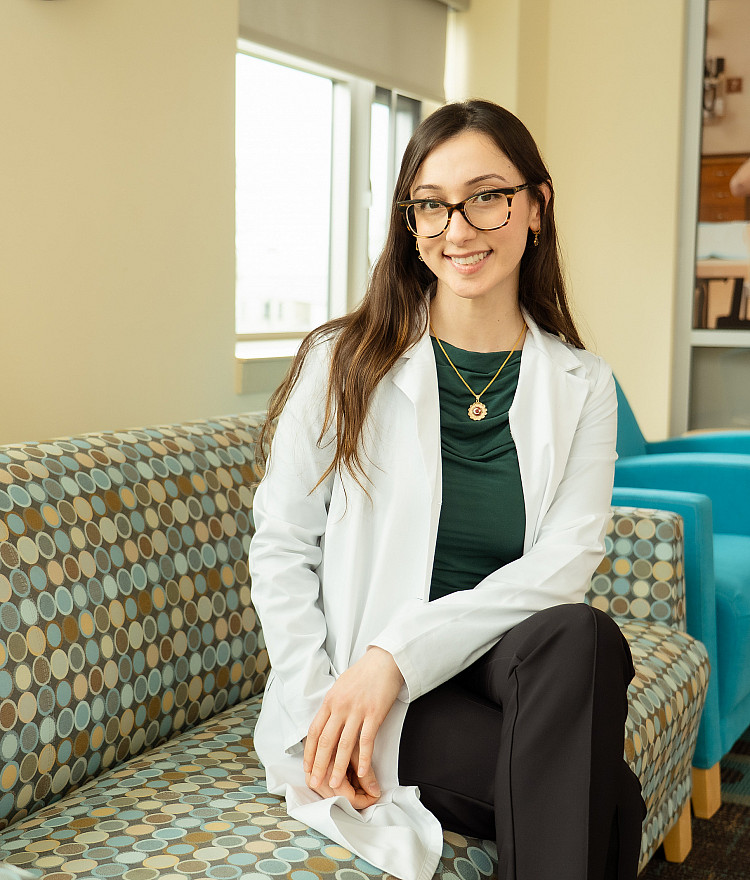 Nursing student sitting on a couch in Lathrop Hall with a white coat on.