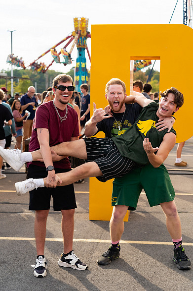 Three Brockport students excitedly celebrating Homecoming Weekend and posing for a group photo at the Homecoming Carnival.