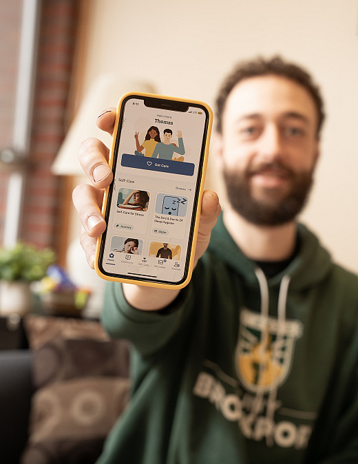 Thomas Messina holding up an iPhone with the TimelyCare app open.