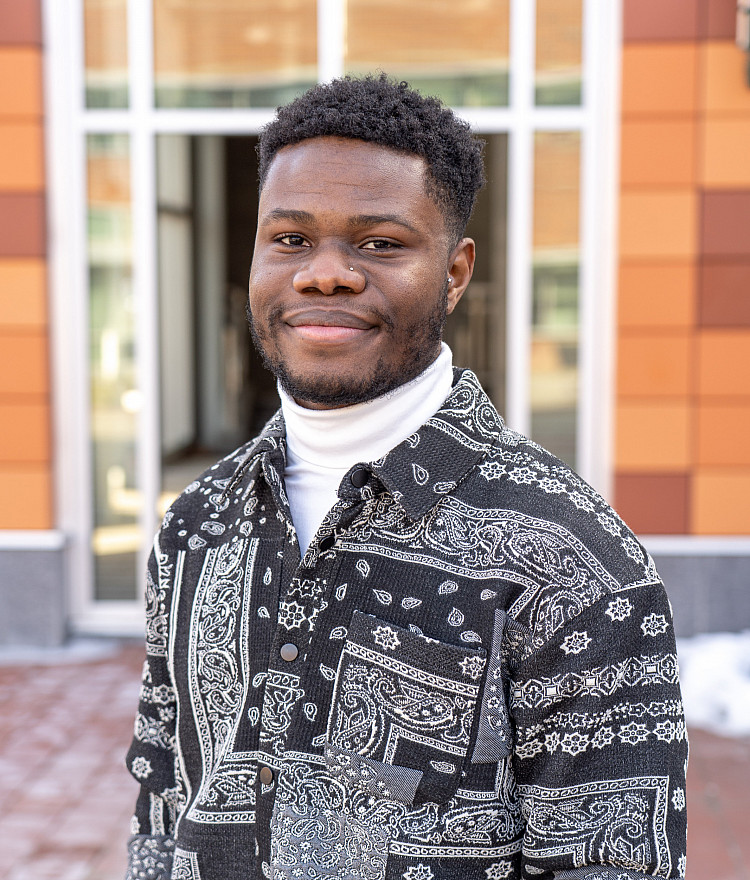 student stands in front of building and smiles
