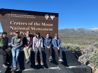 Geology students sitting in front of the Craters of the Moon National Monument sign