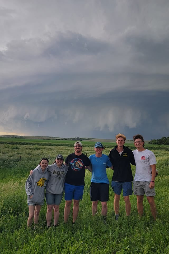 Earth Science students posing in a field with dark grey clouds behind them