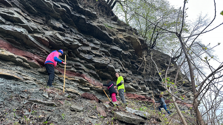 Earth science students facing a rock wall measuring rock layers